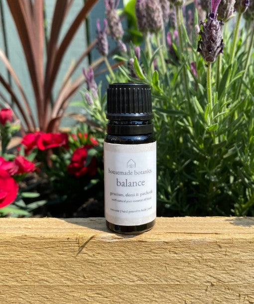 Bottle of 'Balance' essential oil on a wooden surface with flowers in the background