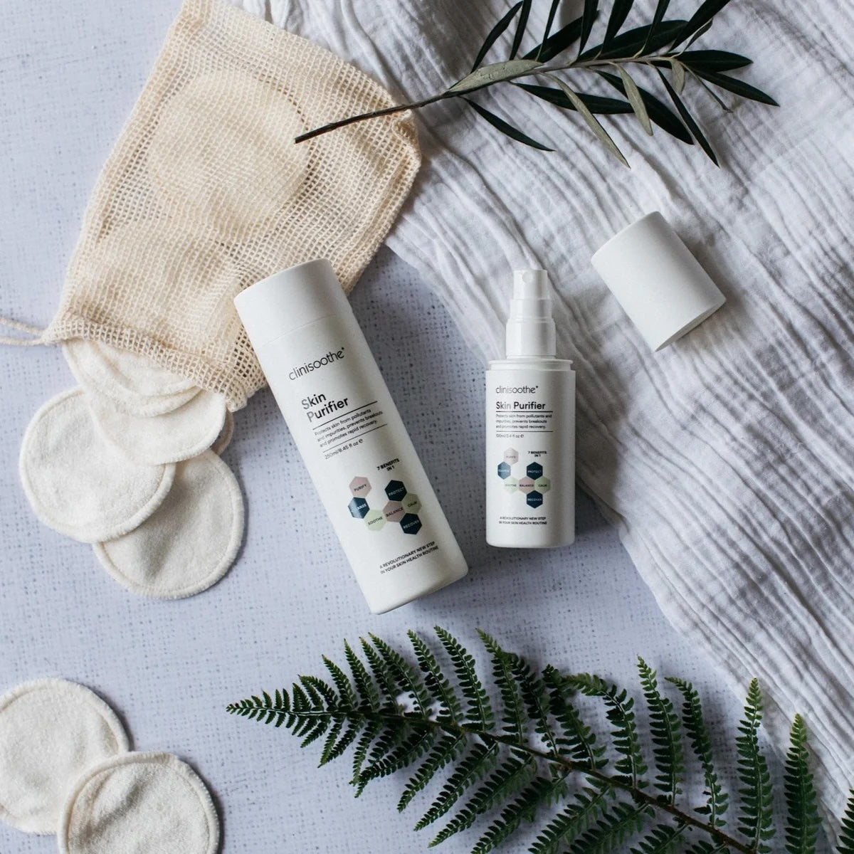 Cosmetic products with cotton pads and fern leaves on a textured surface
