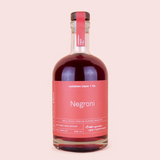 A bottle of Negroni liqueur by Lockdown Liquor & Co. The clear glass bottle is filled with a deep red-brown liquid and features a prominent dusty pink label with white text, sealed with a matching pink neck band and a dark cap, set against a solid pale pink background.
