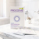 A box of ProCeive Pure Myo-Inositol dietary supplement stands on a marble countertop with two sachets in front, alongside a glass of water and a small potted succulent in a bright kitchen setting.