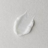 A dollop of thick white cream or lotion on a textured light gray surface.
