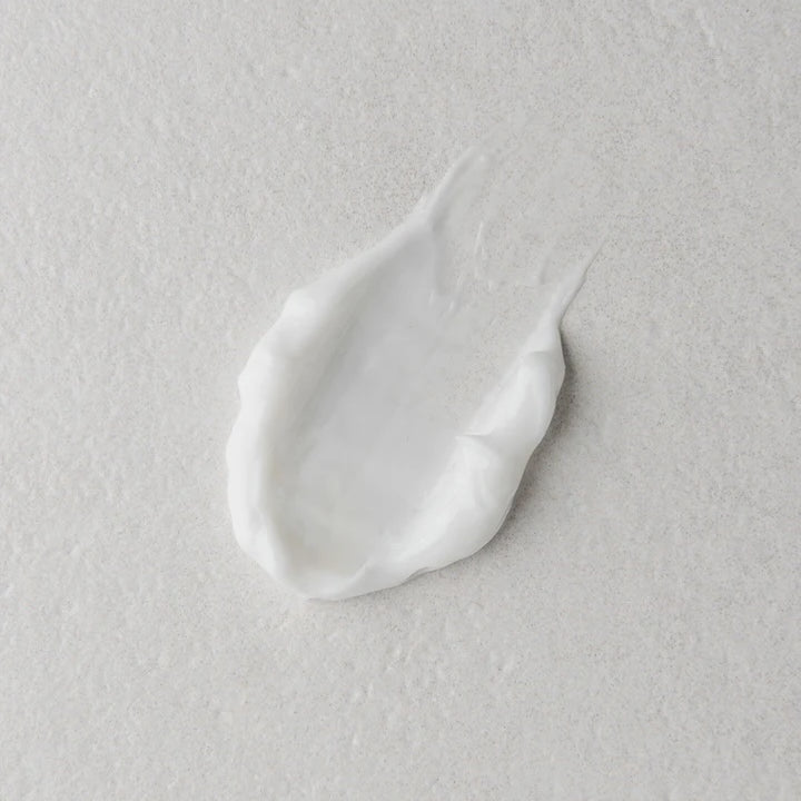 A dollop of thick white cream or lotion on a textured light gray surface.