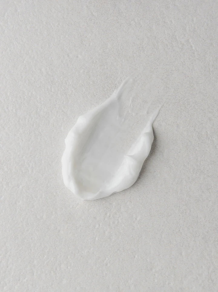 A dollop of thick white cream or lotion on a textured light gray surface.