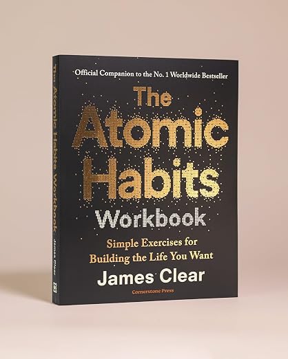 The Atomic Habits Workbook book by James Clear, featuring a black cover with gold and white text, photographed on a neutral beige background.