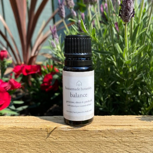 Bottle of 'Balance' essential oil on a wooden surface with flowers in the background
