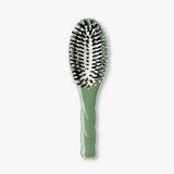 A green hairbrush with black and white bristles, featuring a textured handle and a gold accent at the base, shown on a light gray background.