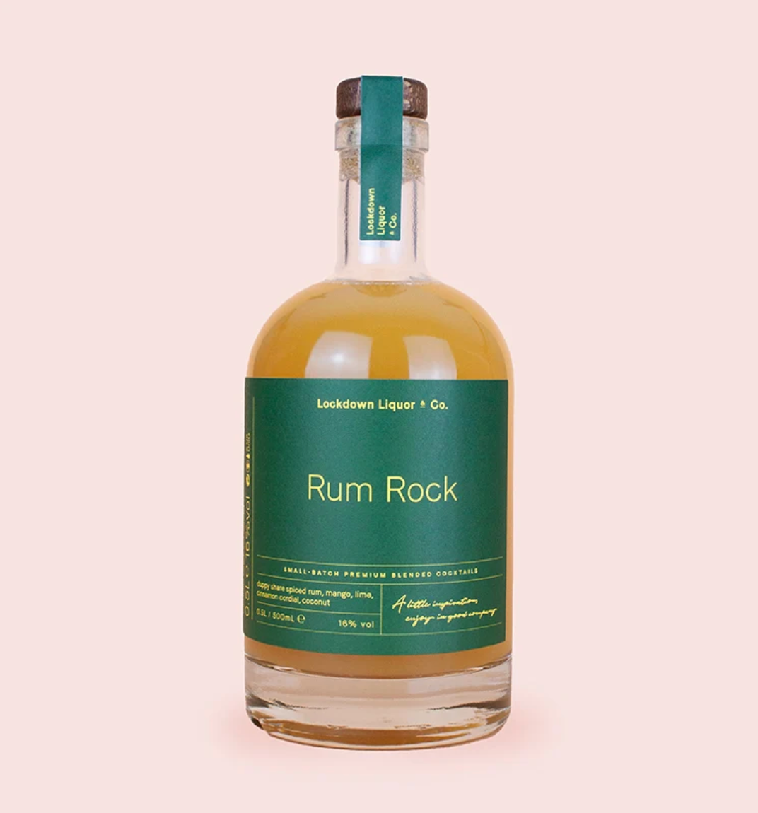 A bottle of Rum Rock by Lockdown Liquor & Co. featuring a dark green label and a brown cork stopper, filled with amber-coloured rum, set against a solid pale pink background.