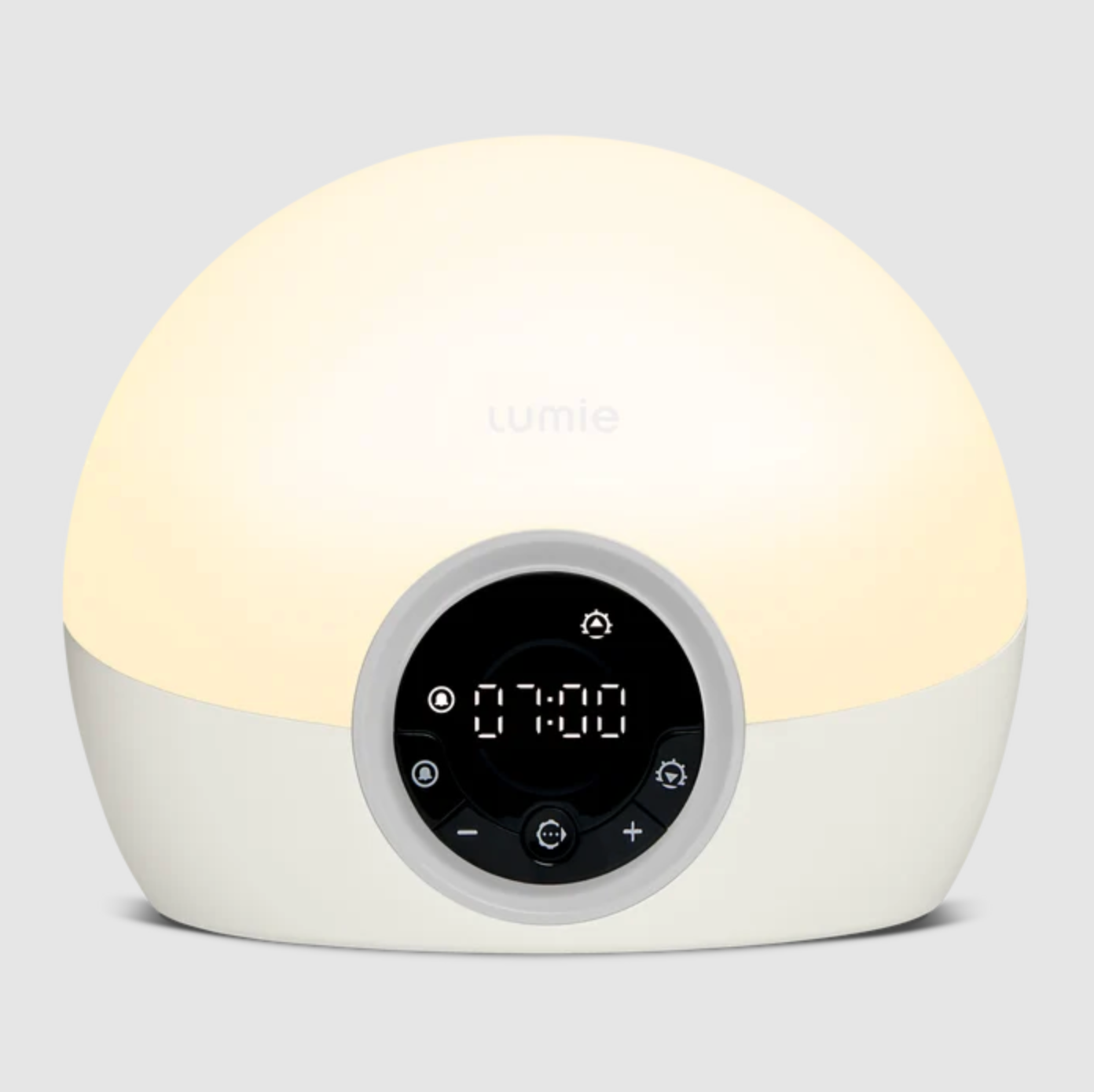 A dome-shaped Lumiie alarm clock lamp with a warm white glowing top half and a white bottom half, featuring a circular black digital control panel on the front.