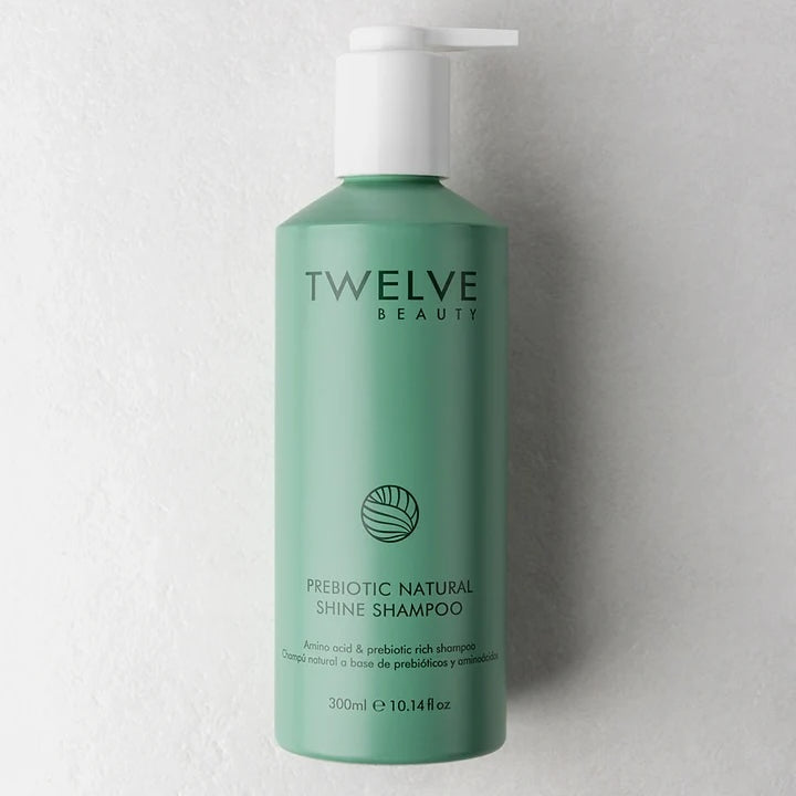 A 300ml bottle of Twelve Beauty Prebiotic Natural Shine Shampoo in a sage green color with a white pump dispenser, set against a textured light gray wall.