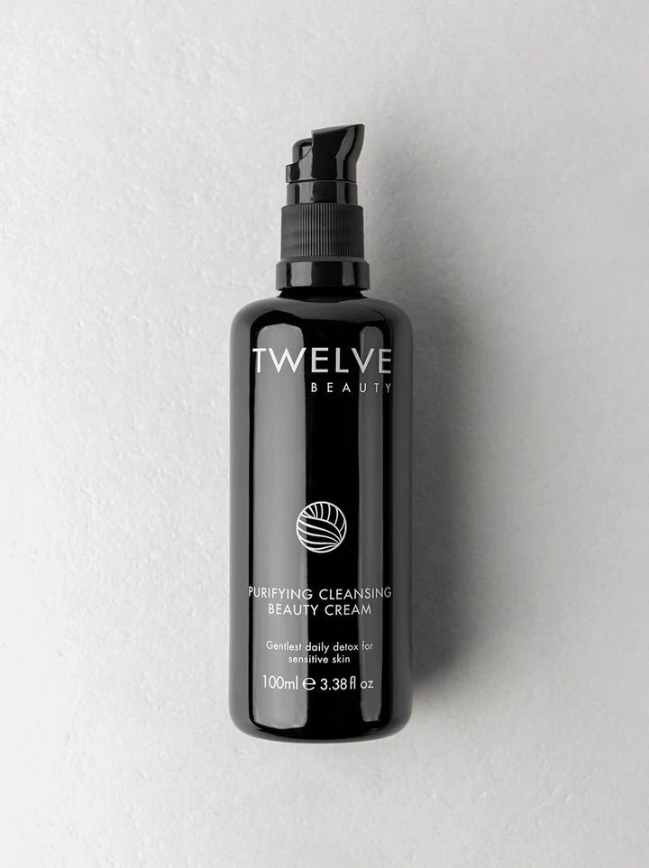 A 100ml black pump bottle of Twelve Beauty Purifying Cleansing Beauty Cream, set against a textured light gray background.